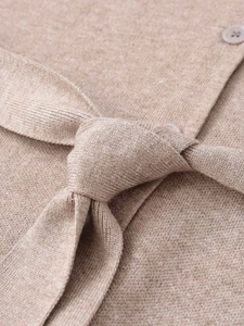 Detail view of beige knitted cardigan showing texture, round button and waist tie knot