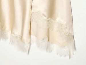 Close-up of champagne satin fabric and intricate white lace hemline on a midi skirt