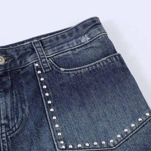 Dettaglio di pantaloncini in denim blu con borchie metalliche e trama del tessuto lavato