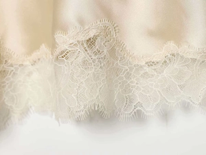 Detail of champagne gold satin skirt with delicate white eyelash lace trim at the hem