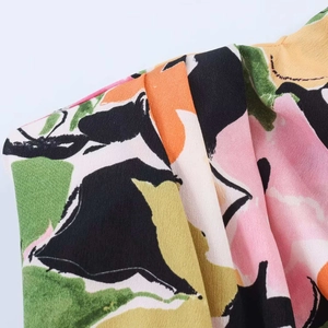 Dettaglio della camicetta in chiffon floreale con spalla a pieghe e motivi astratti vivaci