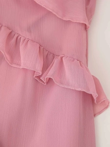Dettaglio dei bordi a balze sovrapposte su un abito estivo in chiffon rosa con trama