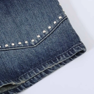Dettaglio in denim blu scuro con rivetti in metallo argento e texture lavata