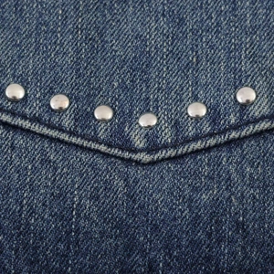Vista dettagliata dei rivetti argentati su tessuto denim blu scuro con trama twill