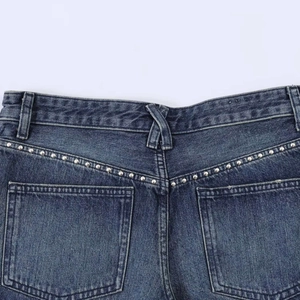 Dettaglio di pantaloncini di jeans blu con borchie argento e cuciture a contrasto