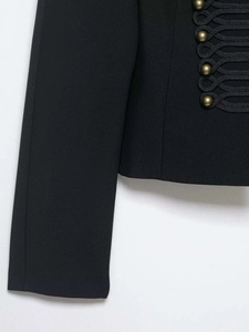 Dettaglio di giacca militare nera con bottoni in metallo bronzo e finiture intrecciate
