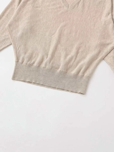 Detail of oatmeal V-neck knit sweater showing fine ribbed hem and batwing sleeve texture
