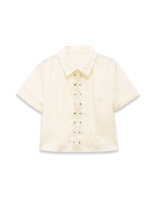 Detail of ruffled trim and metal snap buttons on cream short sleeve shirt