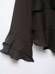 Detail of dark brown layered ruffle sleeves and pleated hem with silky texture