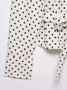Détail du chemisier à pois montrant des poignets larges et une ceinture nouée assortie