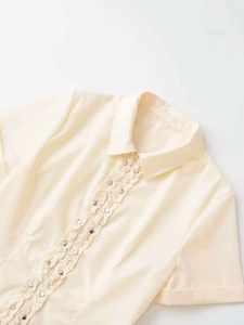 Detail view of ruffled placket with silver buttons on a light yellow short-sleeve shirt