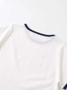 Close-up of contrast crew neck and navy blue ribbed trim on white knit top