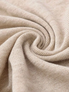 Close-up of soft beige knit fabric with fine needlework texture and soft drapes