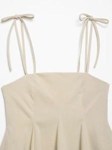 Detail of beige strap top featuring tie-shoulder bows and textured fabric weave