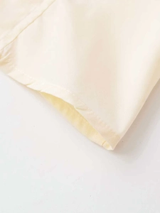 Detailed close-up of rivet studs and rolled edge stitching on a cream cotton shirt