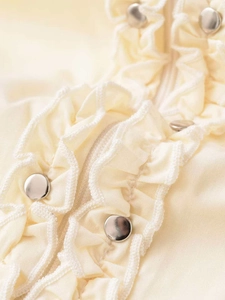Detail view of ruffled shirt layers and polished silver metal buttons on cream fabric