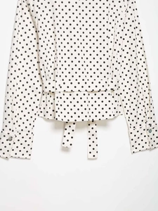 Détail du chemisier blanc à pois noirs avec ceinture à la taille et ourlet à basque chic