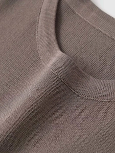 Detailed macro view of the ribbed knit texture and brown crew neck stitching on the sweater