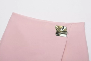 Detail of pink skort featuring an irregular gold metal buckle and pleated fabric texture