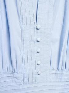 Detail of light blue puff sleeve shirt featuring fabric-covered buttons and pleated texture