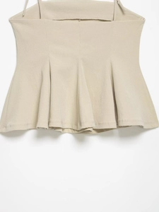 Detail of beige peplum hem top with pleated ruffles and textured lightweight fabric