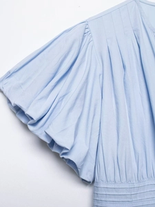 Detail of light blue shirt featuring pleated puff sleeves and intricate smocked waist texture