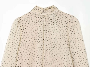 Close-up of beige polka dot chiffon blouse featuring ruffled high collar and long sleeves