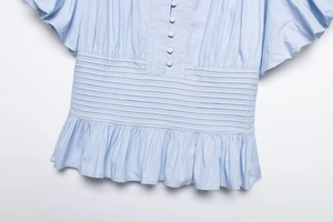 Detailed view of light blue shirt with smocked waist and delicate fabric buttons