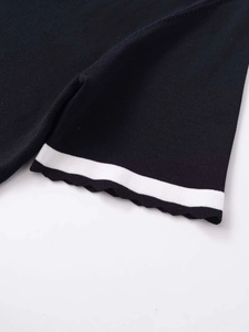 Close-up of black knit top featuring white stripe detail and wavy lettuce edge hem