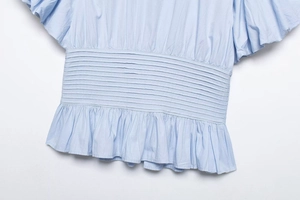 Close-up of pleated waist and ruffled hem on light blue cotton puff sleeve shirt