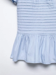 Detail of light blue shirt featuring horizontal pintucks and soft ruffled hem texture