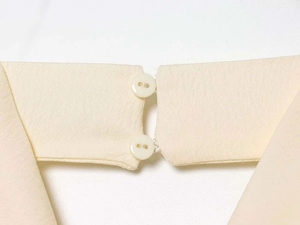 Dettaglio del tessuto beige e due bottoni crema sulla chiusura a girocollo del top