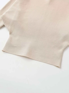 Detail of light beige knitted top showing textured fabric and batwing sleeve structure