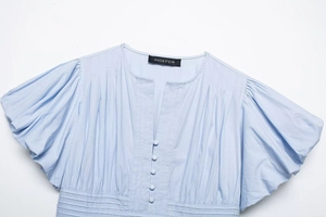 Detail of light blue V-neck shirt featuring pleated puff sleeves and fabric buttons