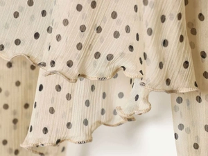 Macro detail of polka dot chiffon fabric with vertical pleats and ruffled edge design