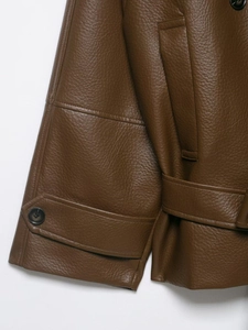 Detail of dark brown faux leather jacket showing lychee grain texture and cuff straps
