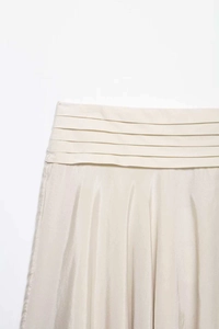 Détail d'une jupe plissée crème à taille haute avec des niveaux horizontaux et texture fine