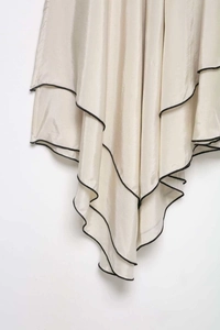 Détail d'une jupe en satin champagne à ourlet irrégulier et liseré noir contrasté