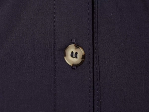 Détail macro du bouton aspect écaille sur le tissu en popeline bleu marine de la robe