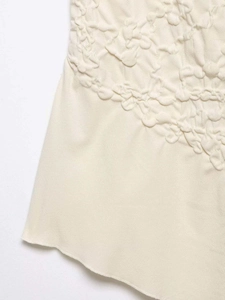Detail of off-white top showing 3D popcorn texture and raw hem edge knit fabric