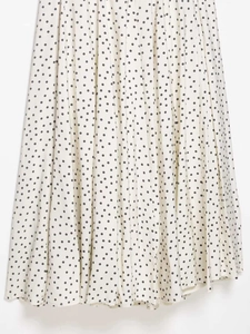 Gros plan détaillé d'une robe midi blanche à pois noirs avec texture de tissu plissé vertical