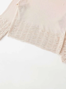 Detailed view of the pleated hem and cuffs on a beige long-sleeve knit sweater