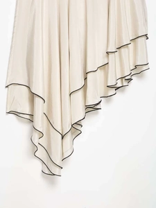 Détail de l'ourlet à volants asymétriques avec liseré noir sur une jupe en satin crème