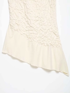 Detail of cream asymmetrical hemline with popcorn textured fabric and smooth stitching
