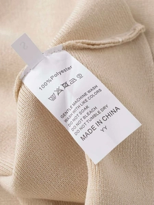 Close-up of care label on beige double V-neck knit sweater showing 100% polyester material