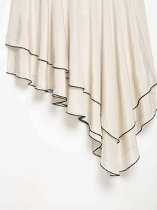 Détail d'ourlet asymétrique avec liseré noir contrasté sur une jupe en satin beige