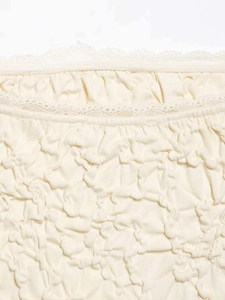 Detail of off-white smocked fabric with delicate lace trim on asymmetric tube top