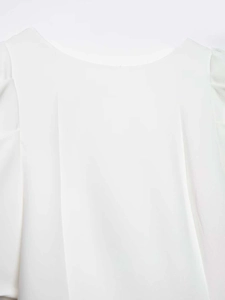 Détail de l'encolure plissée et du design avec nœud en perles sur chemisier blanc