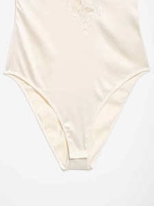 Close-up of cream satin bodysuit with delicate floral lace embroidery and silky texture