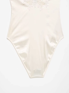 Detail of cream satin bodysuit featuring delicate white floral lace and smooth texture